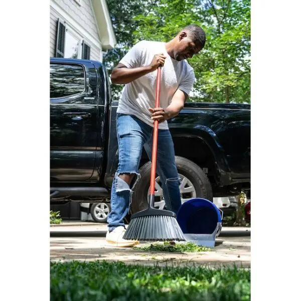 A man is sweeping the driveway with his broom.